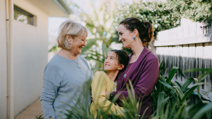 Grandmother, mother and daughter standing in backyard, embracing and smiling